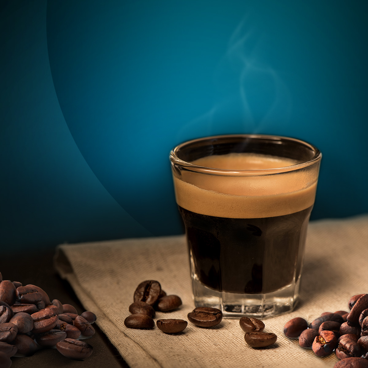 Un bicchiere di espresso con crema poggia su un panno di iuta, circondato da chicchi di caffè su sfondo blu.