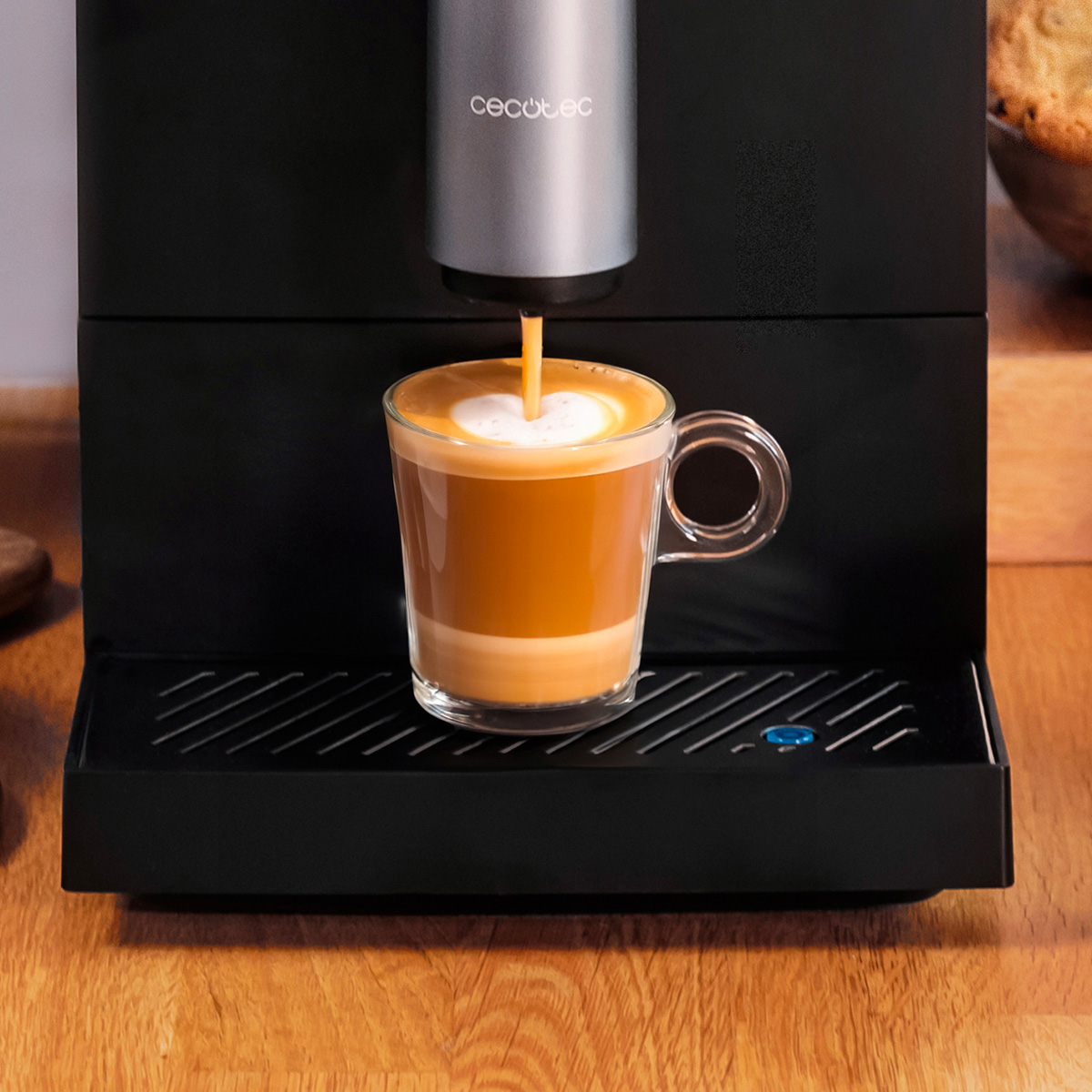 Una macchina da caffè nera Cecotec versa il caffè in una tazza di vetro trasparente con schiuma a strati.