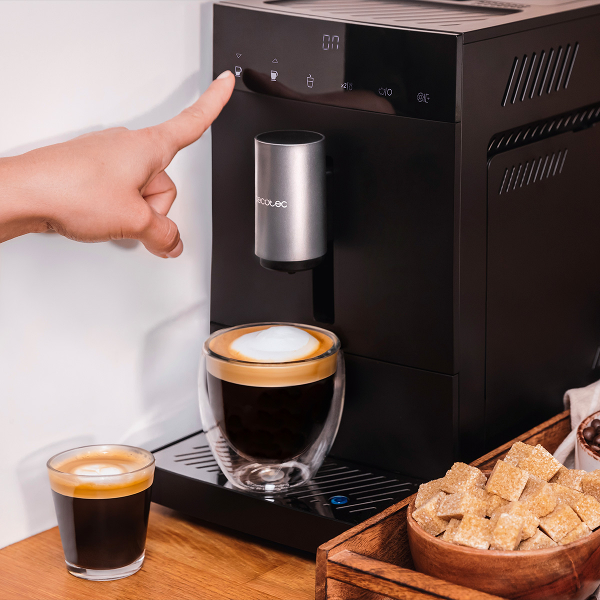 Mano tocca macchina da caffè nera con tazze, bicchiere da espresso e zucchero di canna.