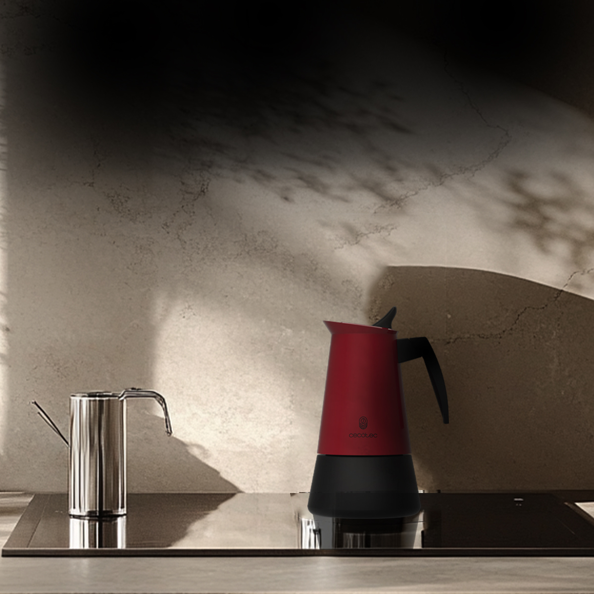 Una moka rossa e nera e un bollitore cromato su un piano cottura contro una parete neutra.