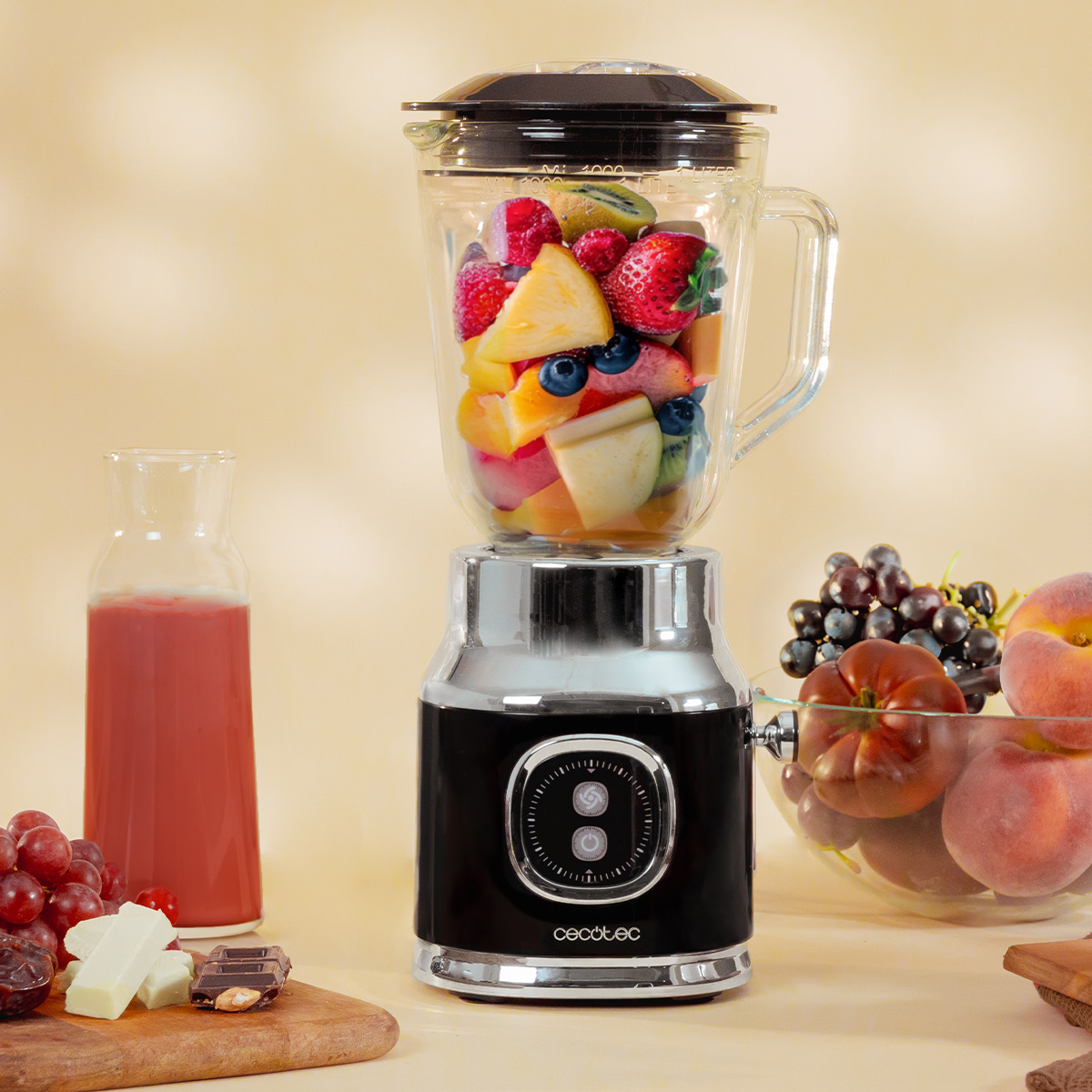 Un frullatore retro nero e cromato pieno di frutta fresca, affiancato da succo, uva e pesche.