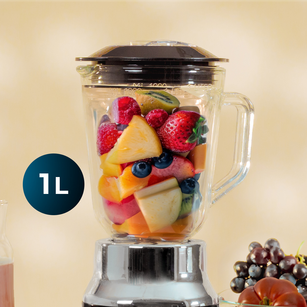 Una licuadora de vidrio llena de frutas frescas y coloridas se encuentra ante un fondo claro con un marcador de 1L.