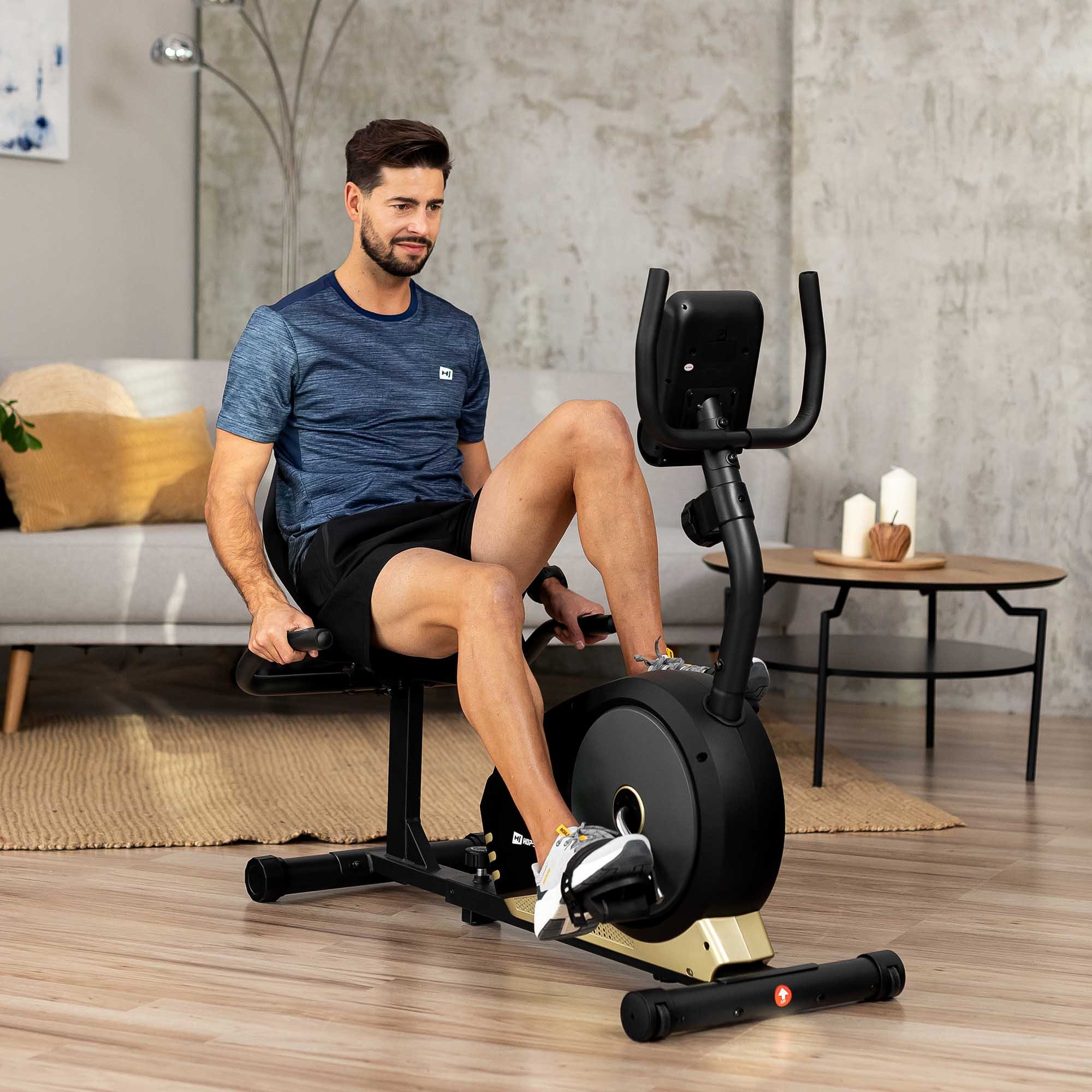 Ein Mann trainiert im Wohnzimmer auf einem schwarzen Liegeheimtrainer.