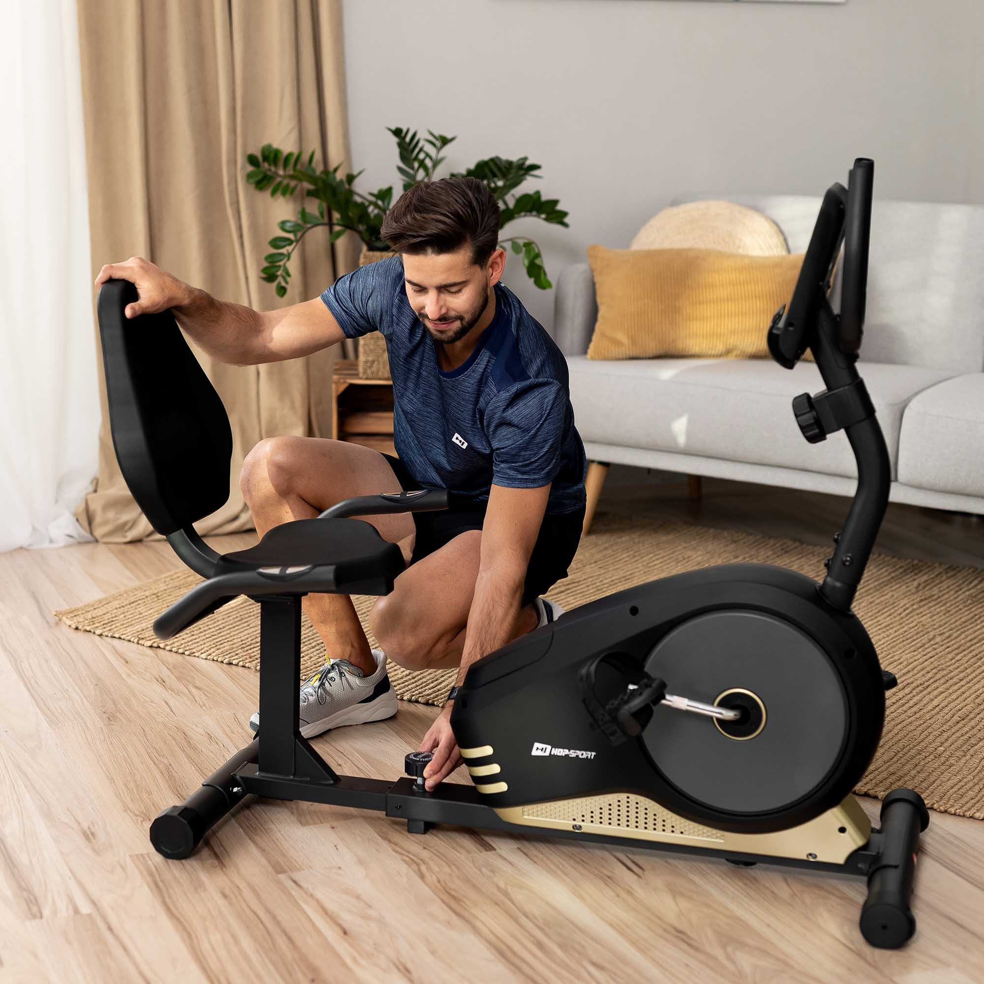Ein Mann in Sportkleidung stellt einen Heimtrainer in einem hellen Wohnzimmer ein.