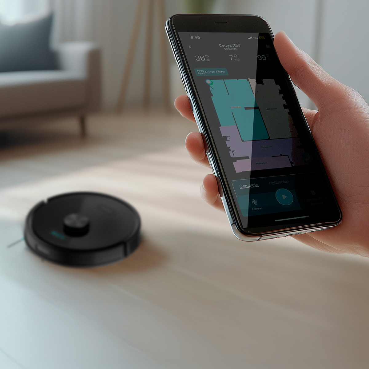 Una mano sostiene un teléfono con una app de aspiradora robot, y una aspiradora robot negra en el suelo al fondo.