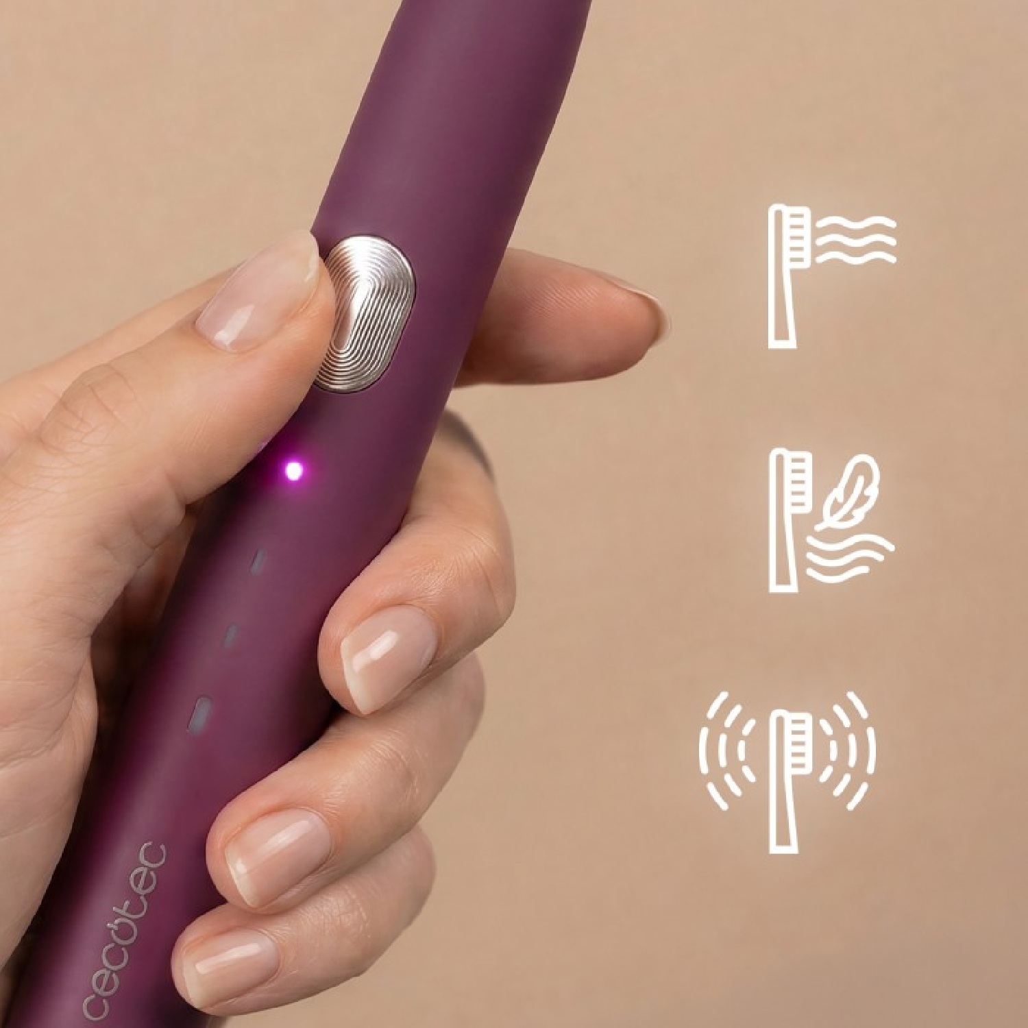 Mano sosteniendo un cepillo de dientes eléctrico morado con un botón plateado y tres iconos de modo a la derecha, sobre fondo beige.