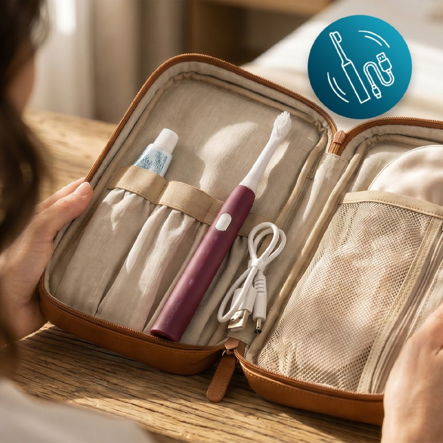 Un estuche de viaje marrón abierto contiene un cepillo de dientes eléctrico granate, pasta y un cable USB.