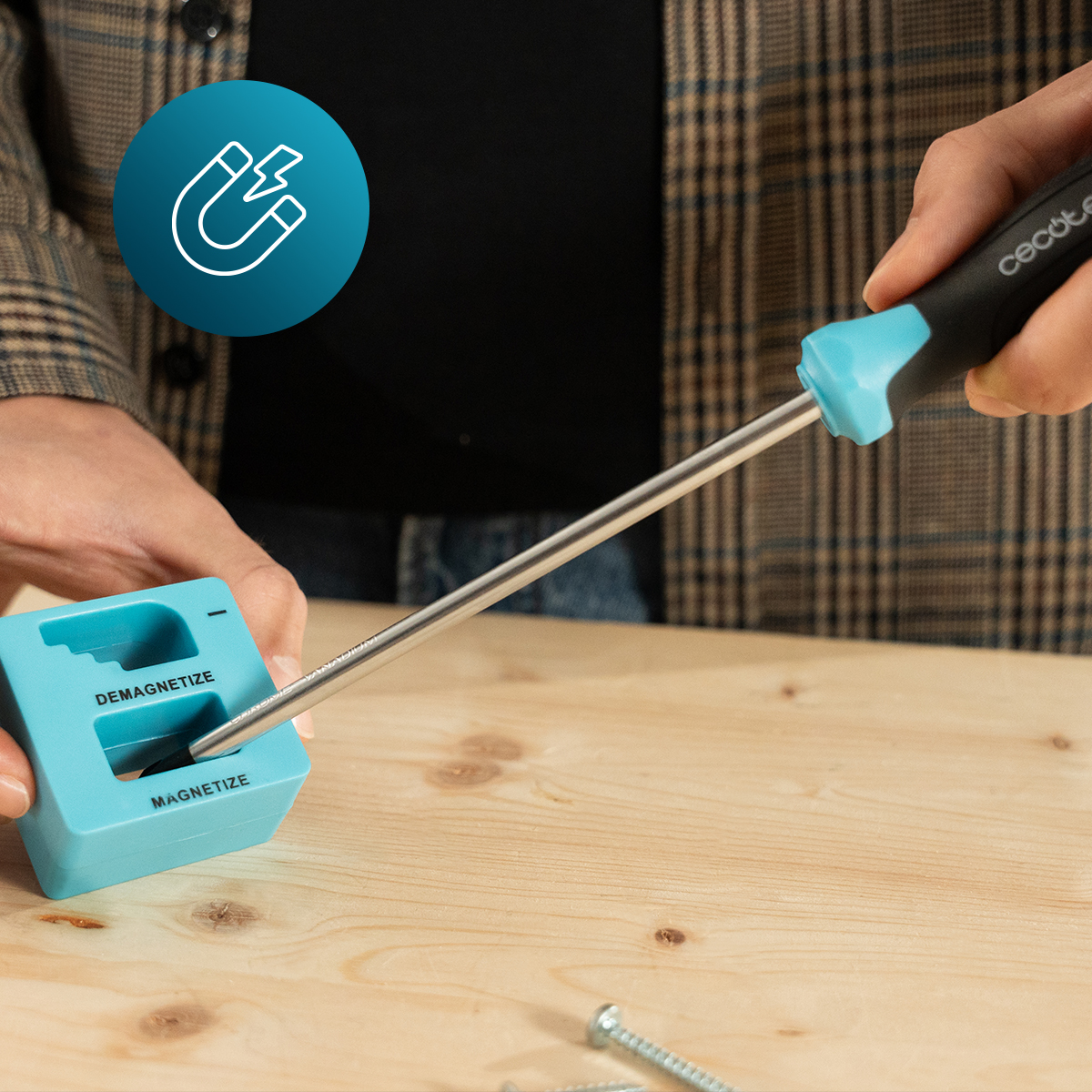 Una mano magnetiza un destornillador en un imantador azul sobre una mesa.