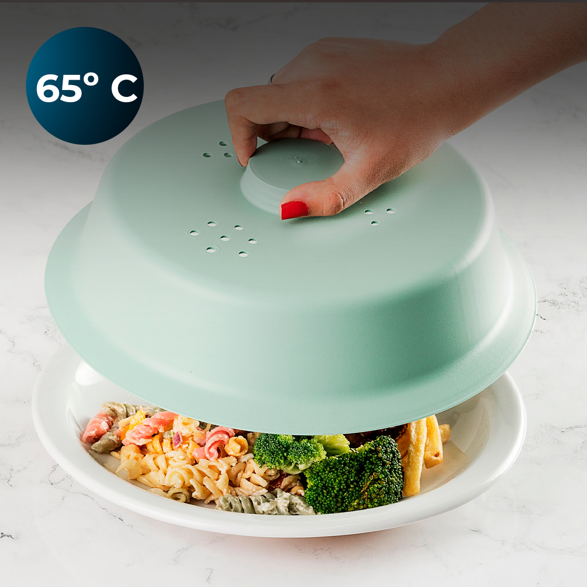 Una mano cubre un plato de pasta y brócoli con una tapa verde menta.