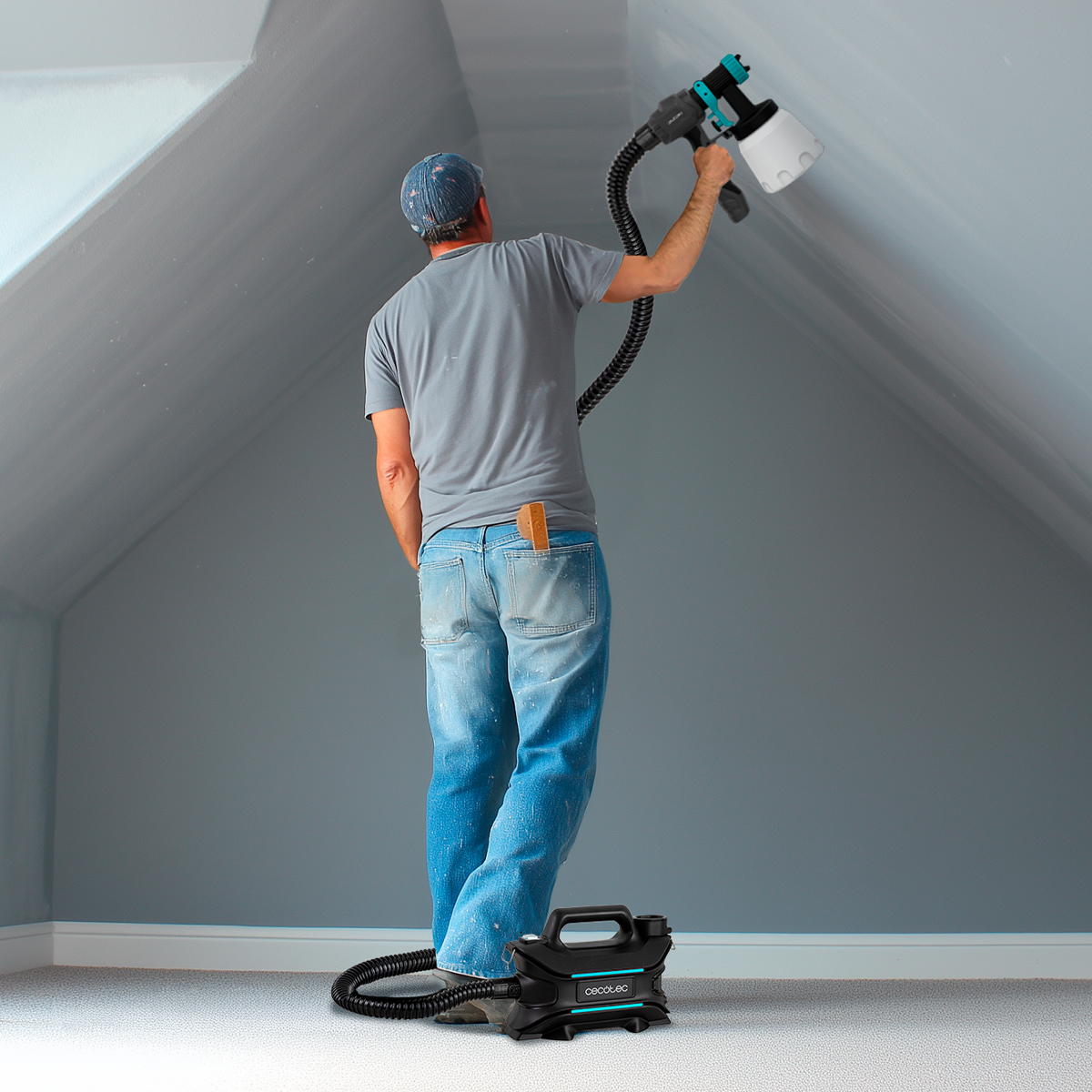Un pintor usa un pulverizador eléctrico para pintar el techo gris de una habitación.
