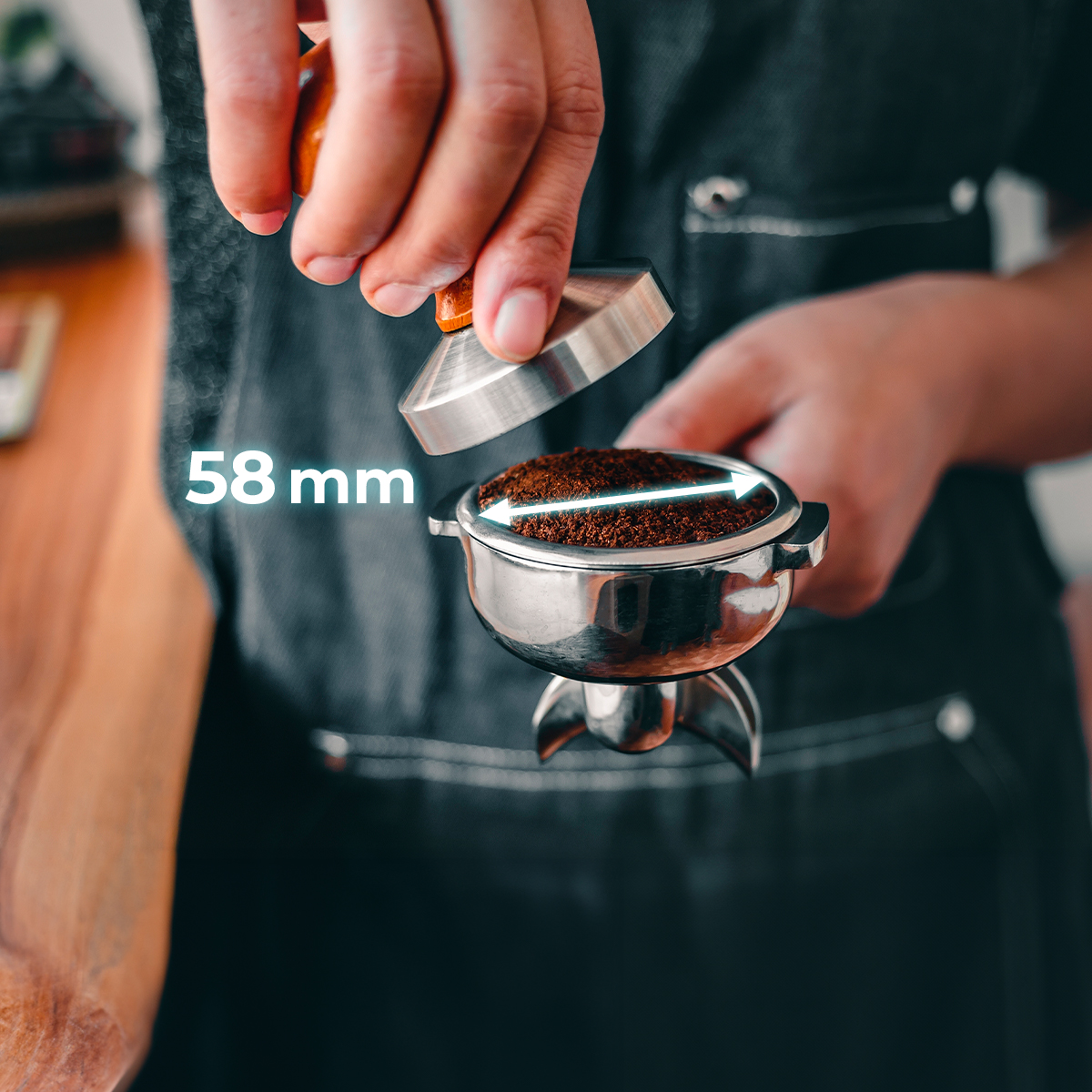 Un barista compacta café molido en un portafiltro de 58 mm con un tamper.