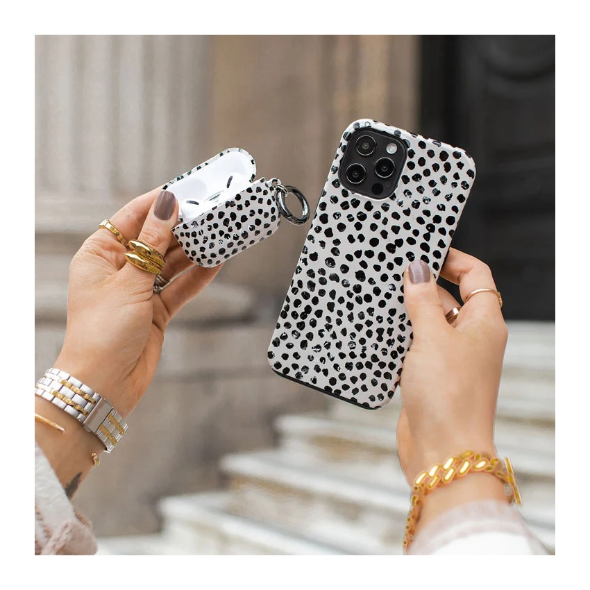 Hands holding a matching black-and-white speckled phone case and AirPods case, accessorized with gold jewelry.