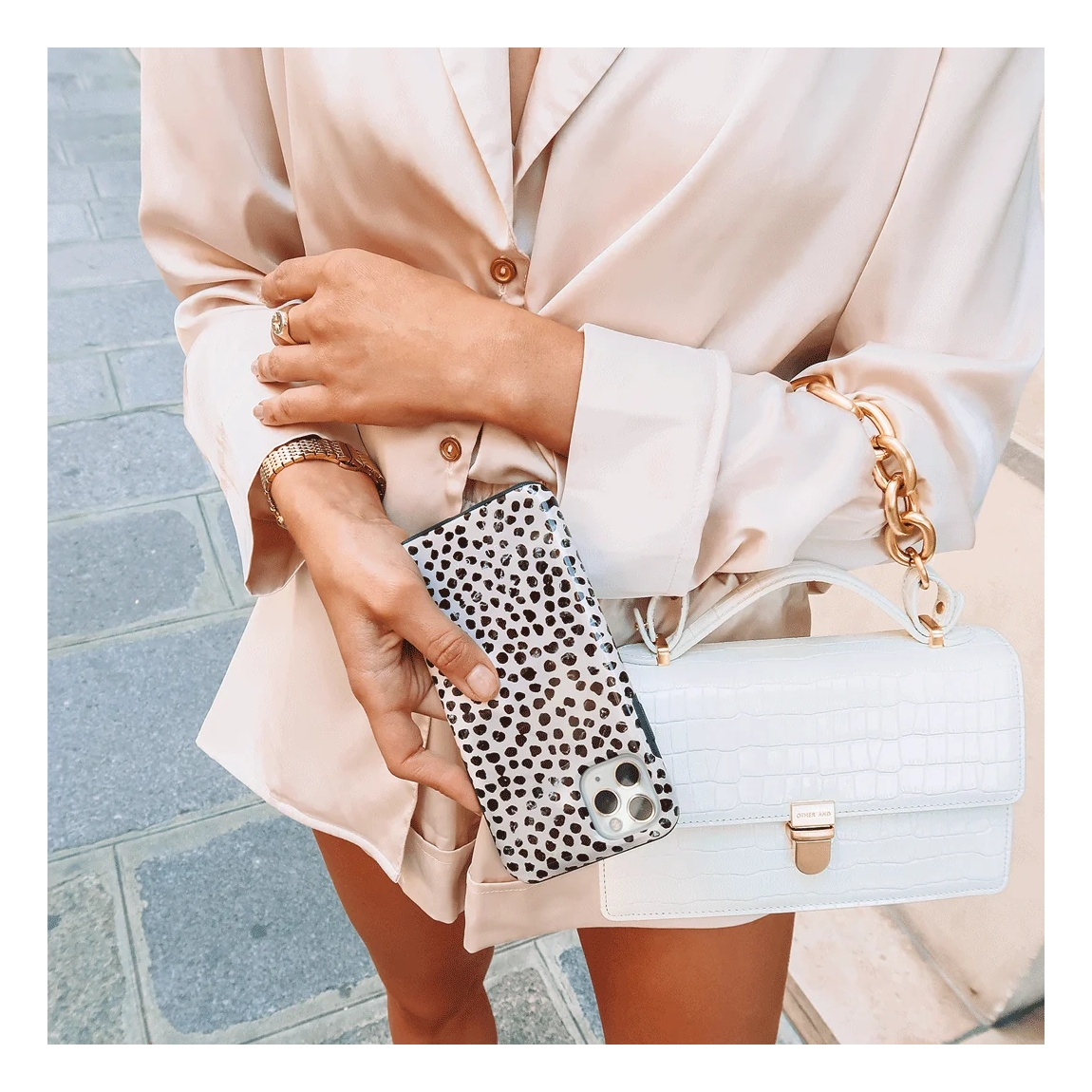 A person in a beige silk shirt holds a leopard-print phone and a white handbag.