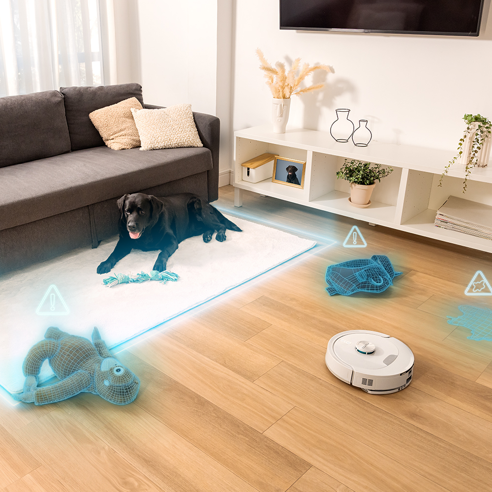 Un robot aspirador limpia el suelo mientras un perro negro descansa sobre una alfombra.