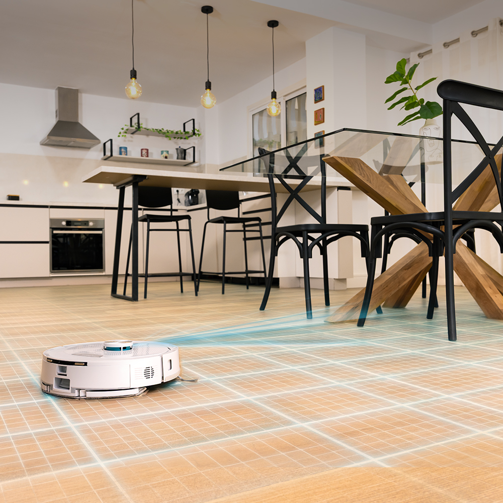 Un robot aspirador blanco limpia un suelo de baldosas en una cocina y comedor modernos.