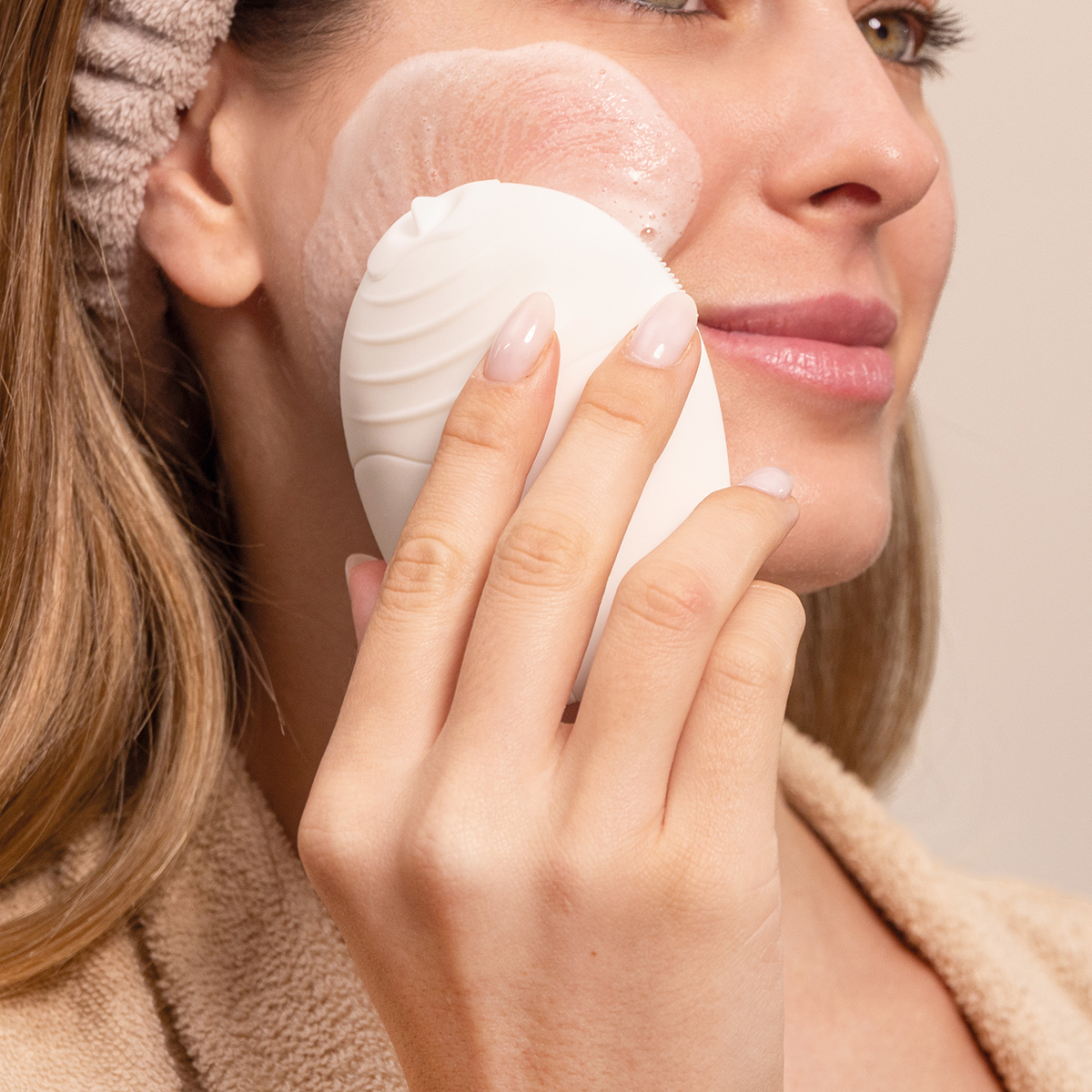 Una donna pulisce il viso con una spazzola detergente bianca in silicone e schiuma.