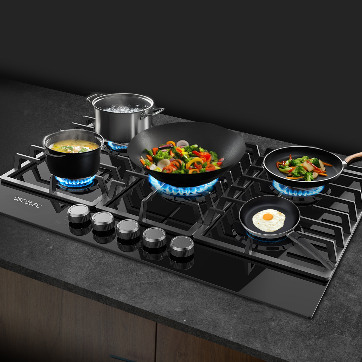 Placa de gas negra con llamas azules bajo ollas, wok y sartenes cocinando verduras y un huevo.