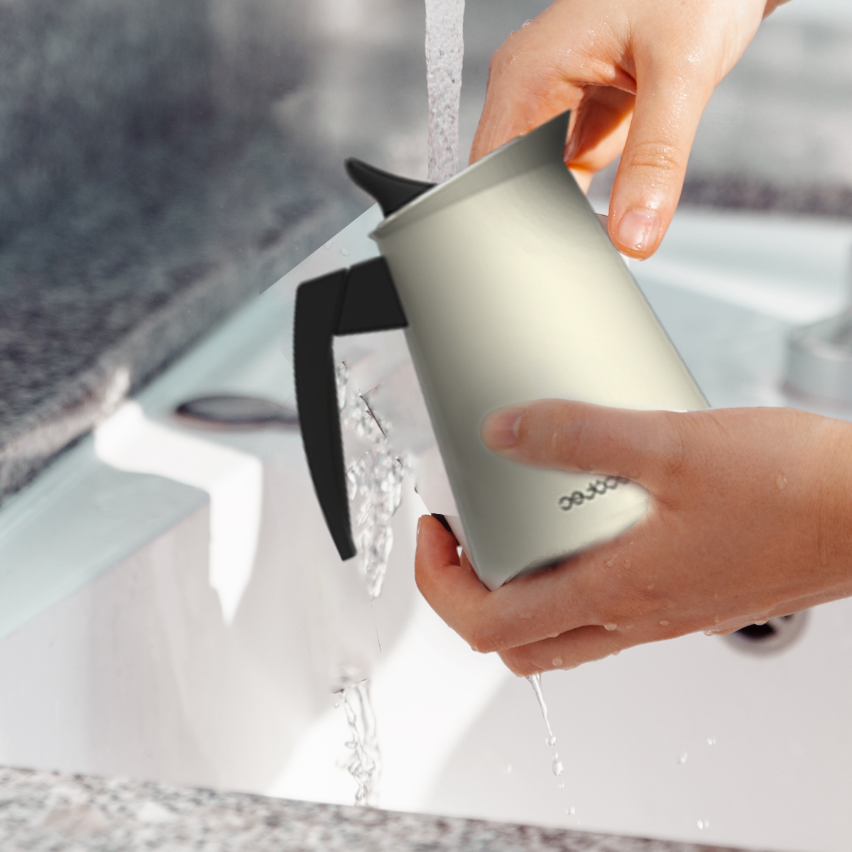 Mani che lavano una caffettiera grigia sotto l'acqua corrente in un lavandino.