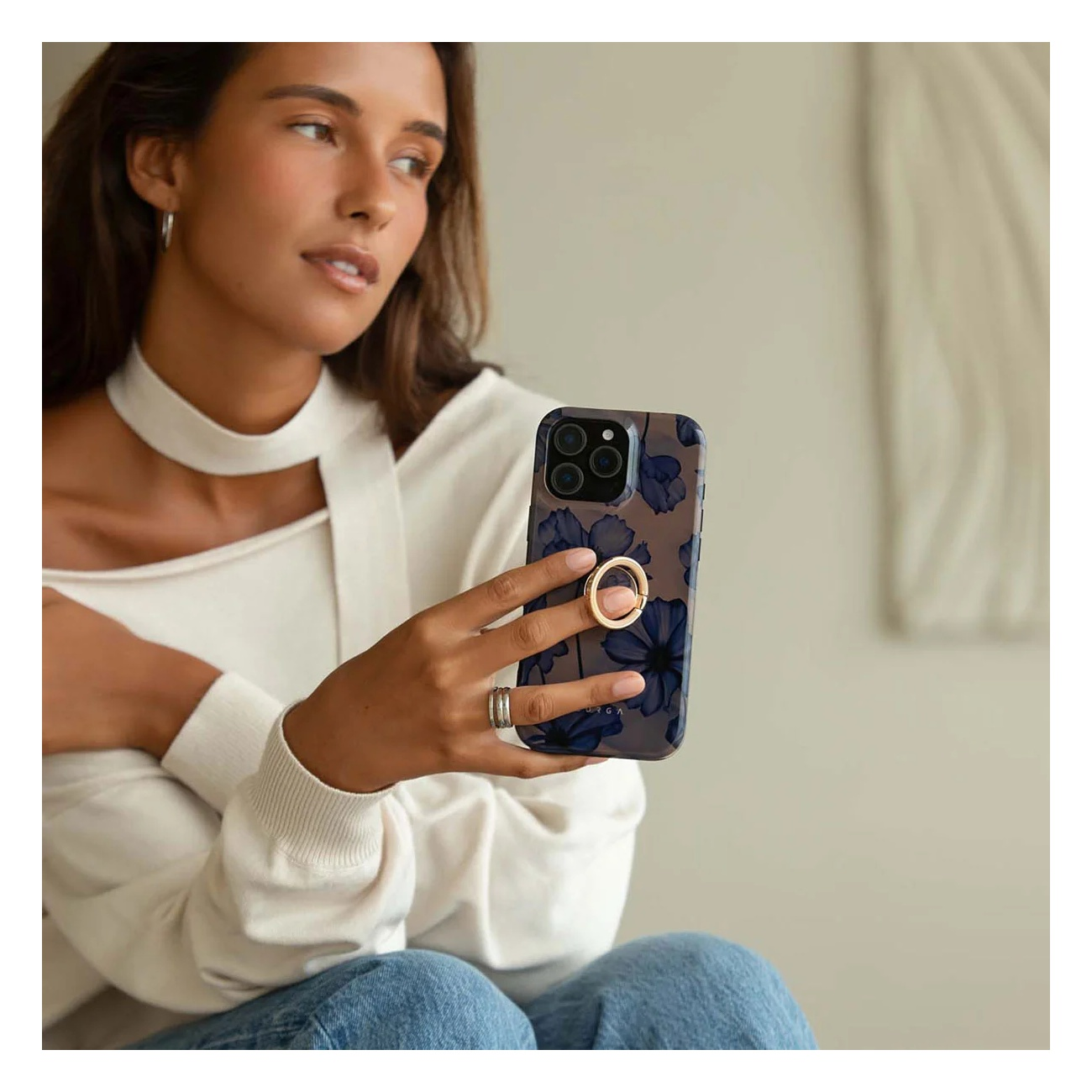A woman in a white top holds a blue smartphone with a floral pattern and a gold ring holder.