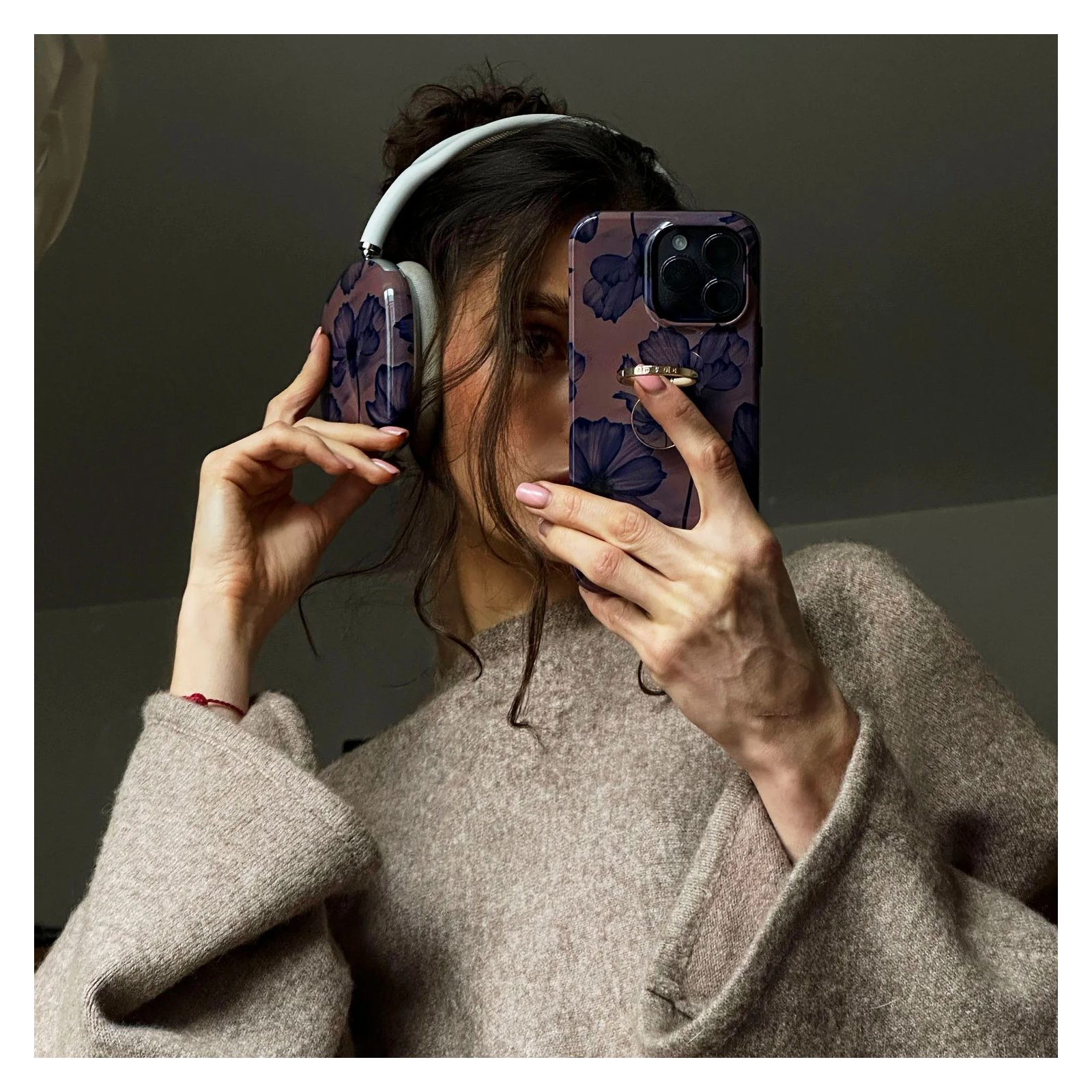 A woman in a beige sweater holds a smartphone with a floral case, wearing matching floral headphones.