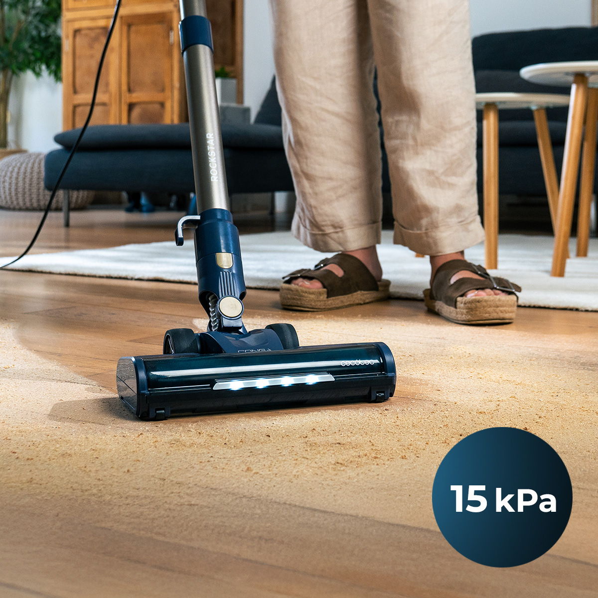 Una persona aspira un pavimento in legno con un aspirapolvere blu cordless in salotto.