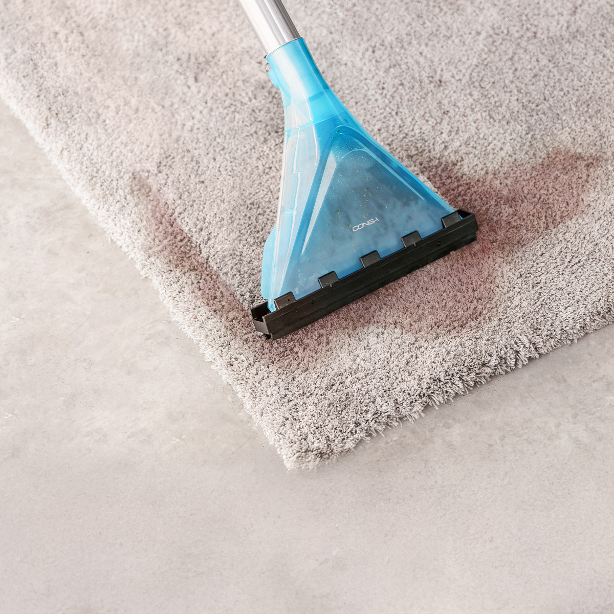 Un accessorio per aspirapolvere blu pulisce un tappeto grigio macchiato.