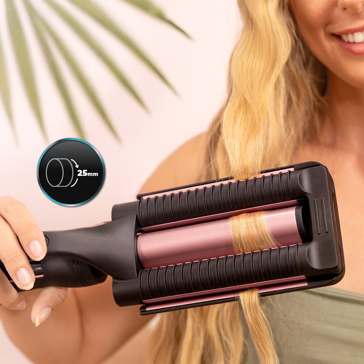 Una donna usa un ferro arricciacapelli rosa e nero da 25 mm sui capelli biondi, con una foglia di palma sullo sfondo.