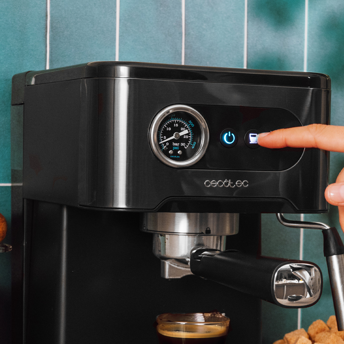 Una mano preme il pulsante di erogazione su una macchina da caffè nera con manometro.