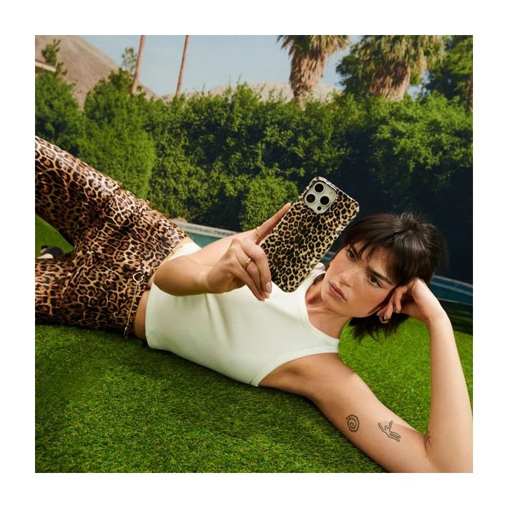A woman in leopard print pants lies on grass, holding a matching phone.