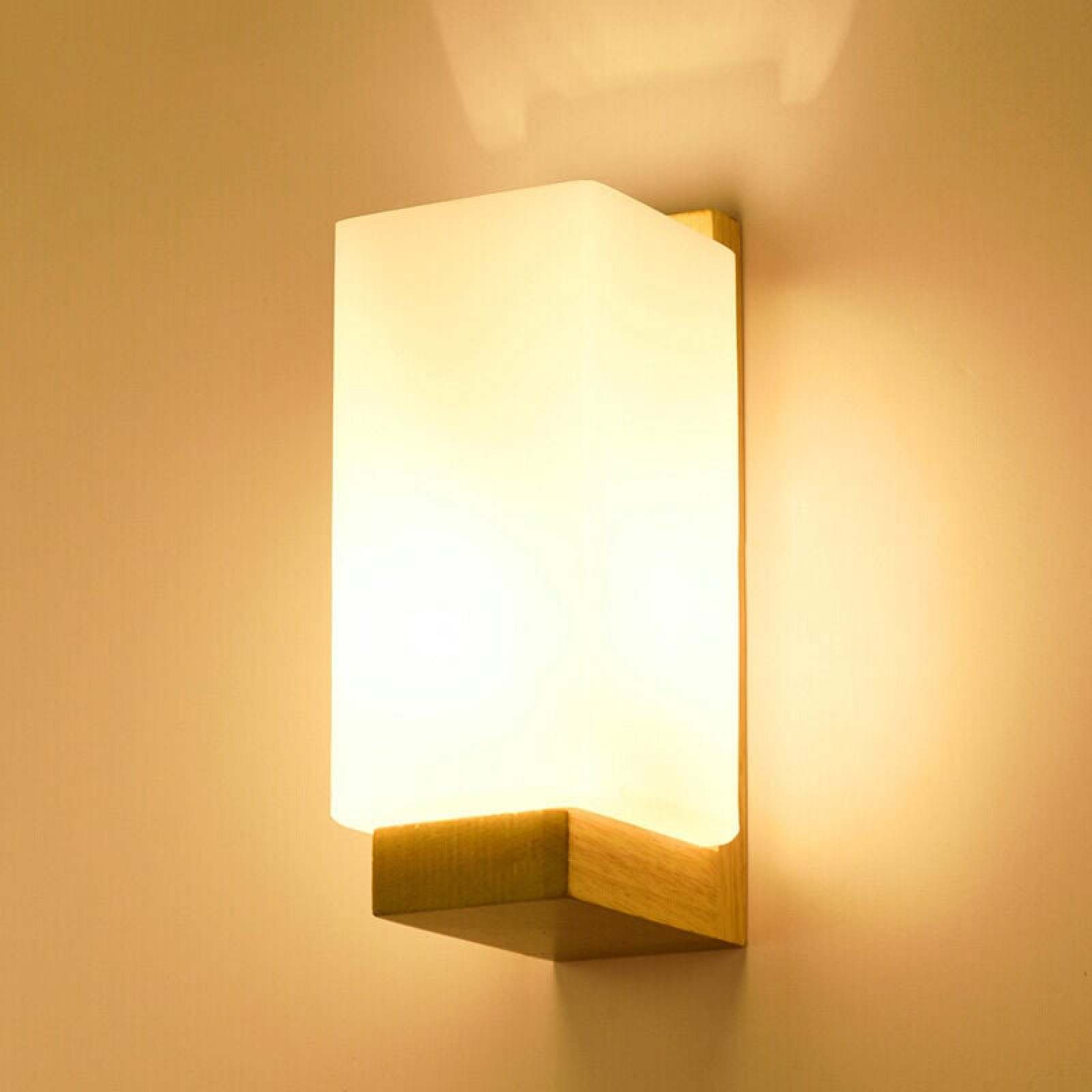 Eine moderne Wandleuchte mit einem rechteckigen Glas und Holzhalterung leuchtet warm an einer beige Wand.