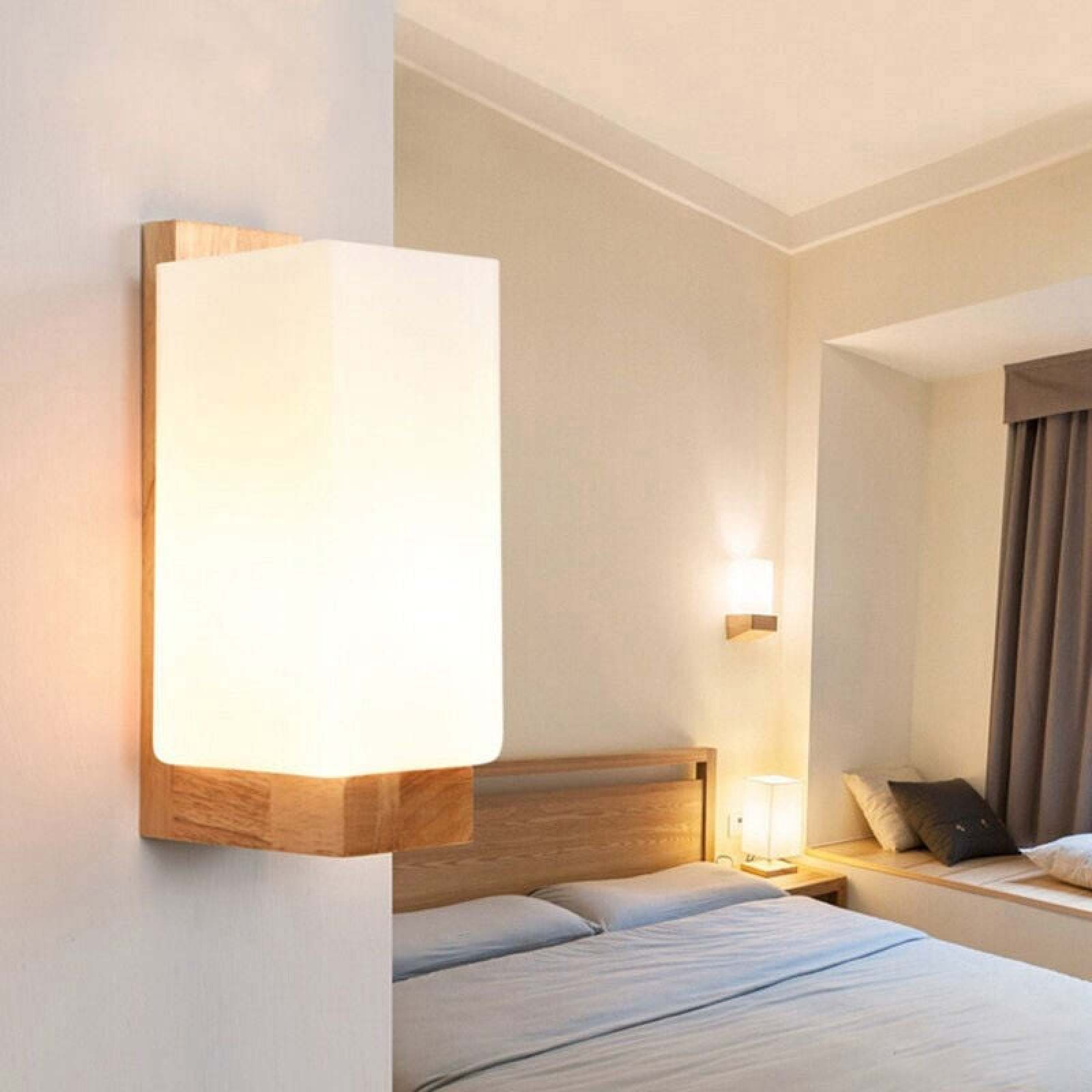 Eine moderne Wandlampe aus Holz mit weißem Schirm in einem Schlafzimmer mit Bett und Fenster.