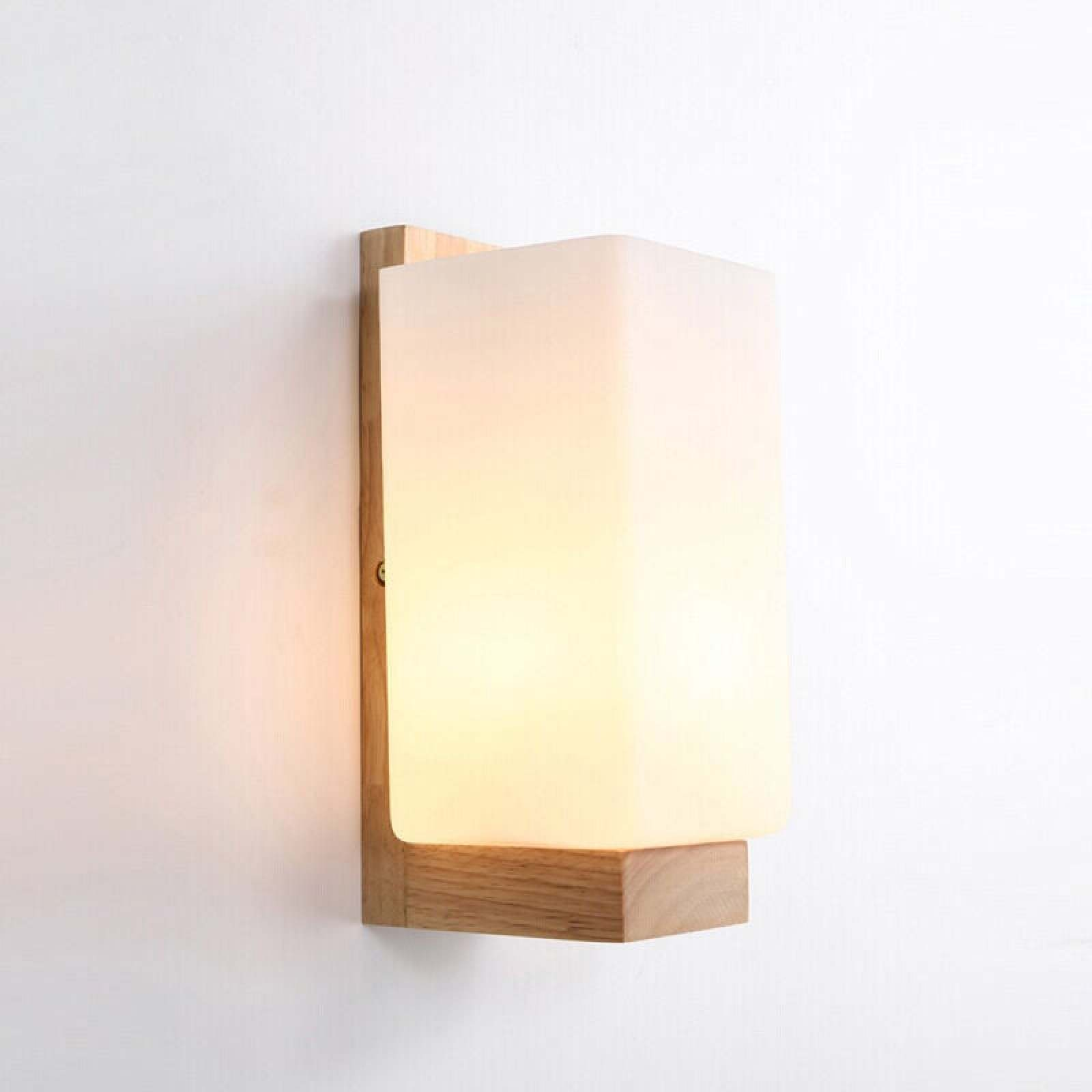 Eine moderne Wandleuchte mit hellem Holzhalter und mattem Glasschirm strahlt warmes Licht aus.