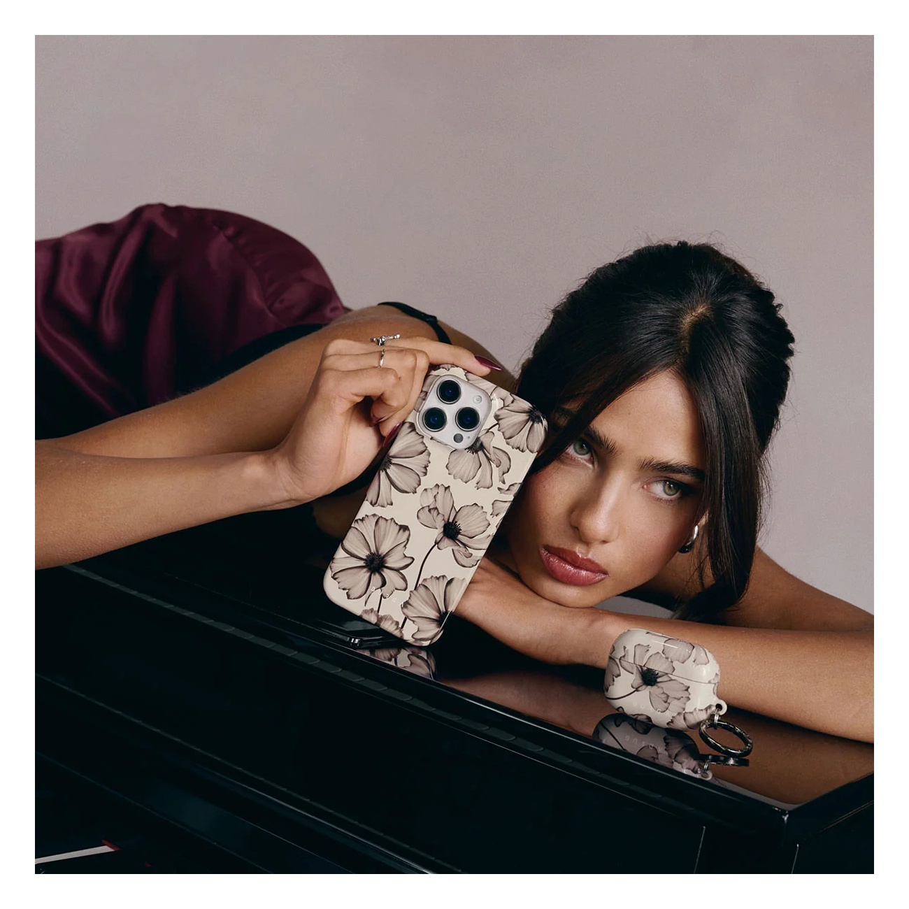 A woman lies on a piano, holding a phone and a case with a floral pattern.