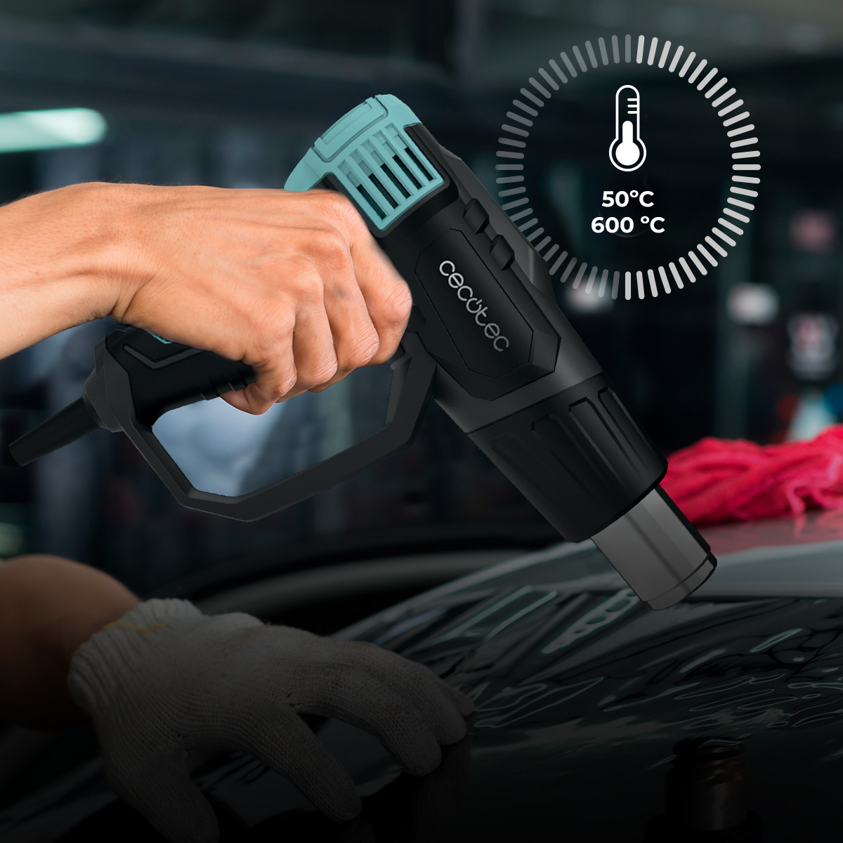 Una mano sostiene una pistola de calor Cecotec negra y turquesa con indicador de temperatura.