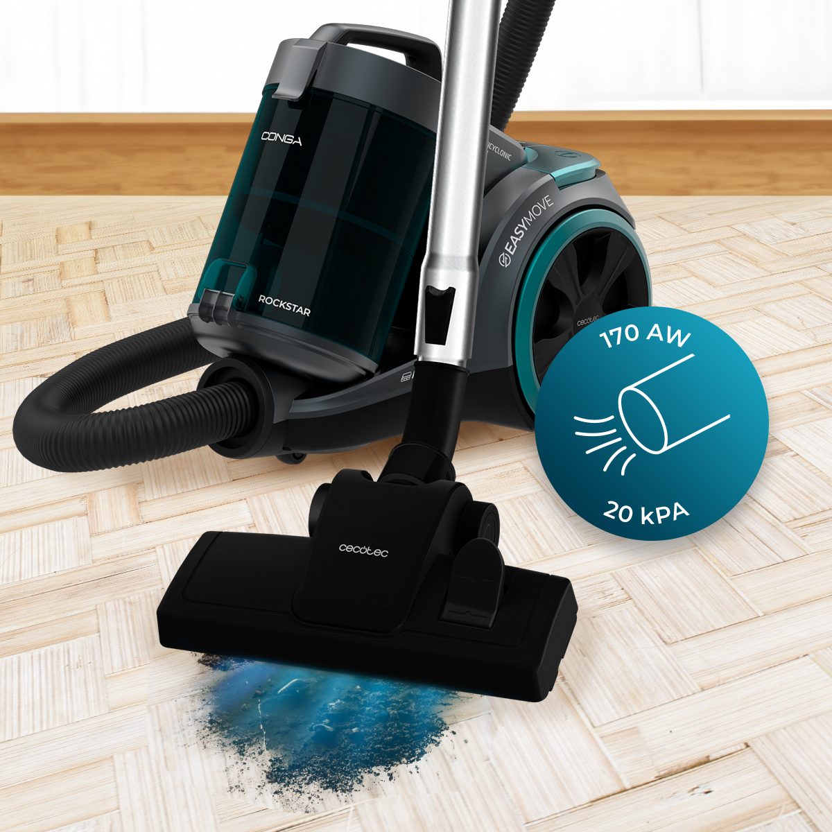 Un aspirapolvere grigio con serbatoio blu è su pavimento in legno e pulisce una macchia.