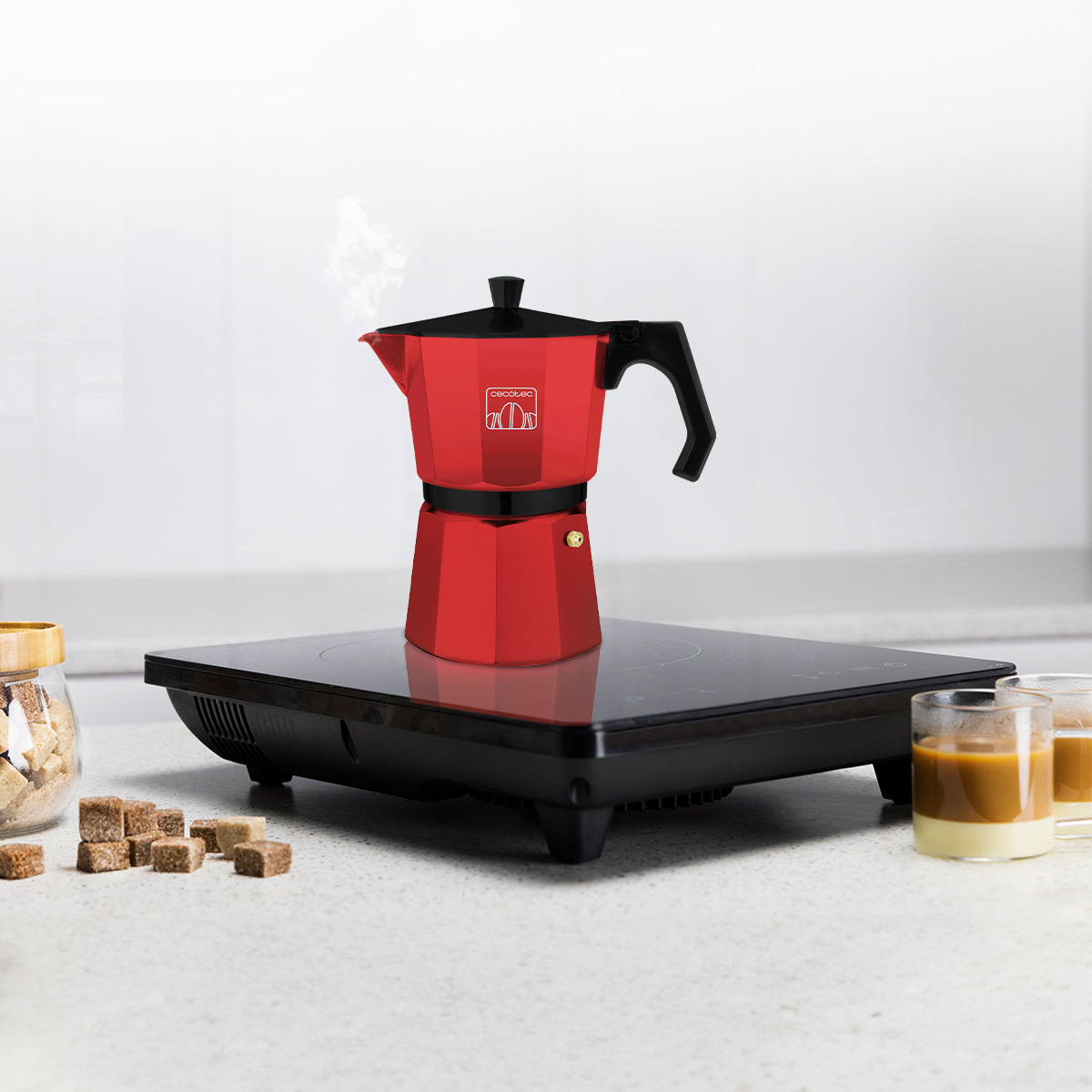 Una moka rossa e nera su un piano cottura elettrico con caffè fumante, zucchero e bicchieri.