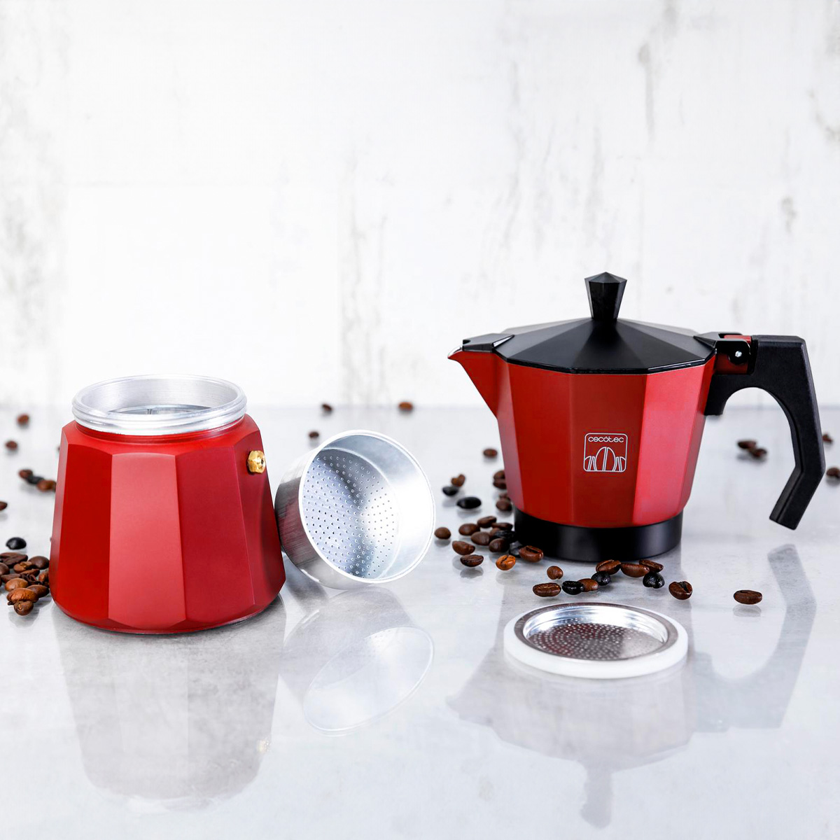 Una caffettiera moka rossa smontata con chicchi di caffè su un tavolo.