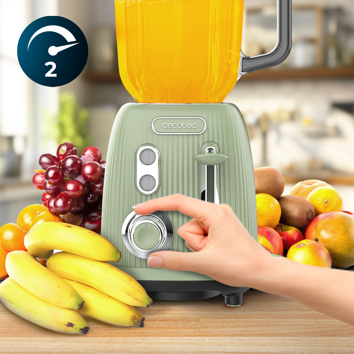 Una mano gira el dial de una licuadora Cecotec verde menta, rodeada de frutas frescas como plátanos y uvas.
