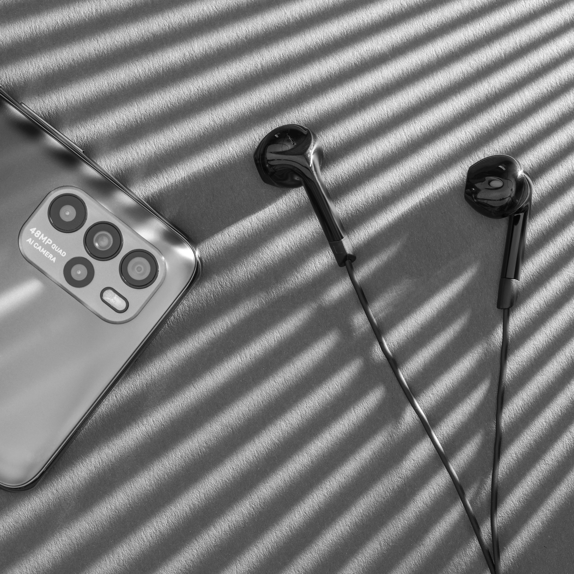 Szary widok z góry przedstawia smartfon z poczwórnym aparatem i słuchawki przewodowe na powierzchni w paski.