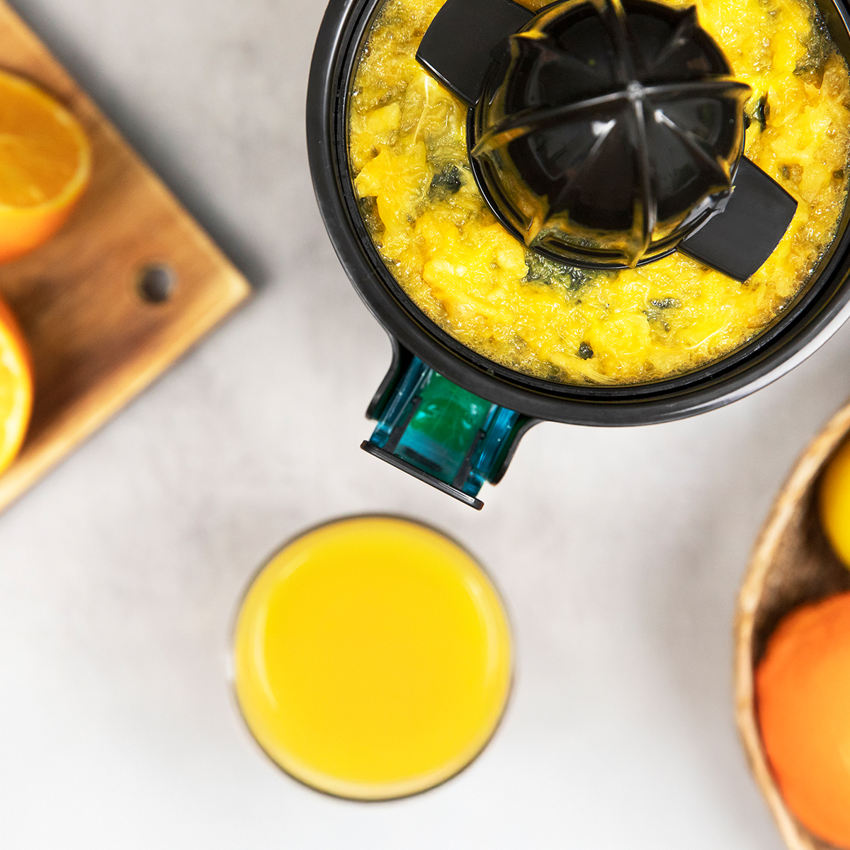 Un exprimidor negro con pulpa de cítricos amarillos, un vaso de zumo de naranja recién exprimido y una tabla de cortar de madera.