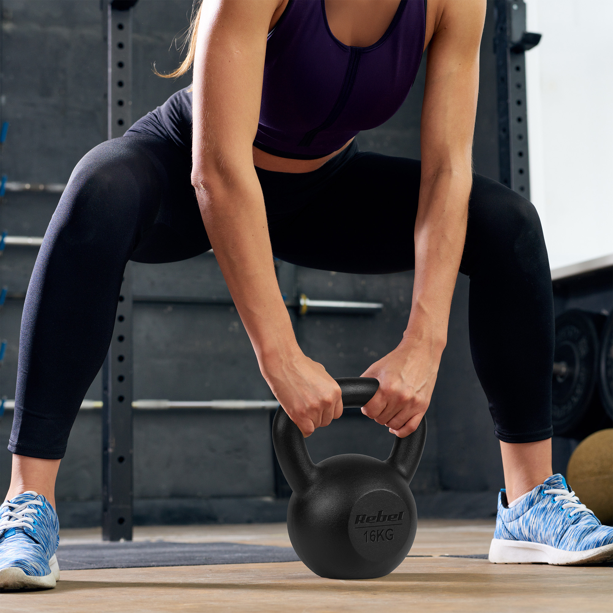 Kobieta w stroju sportowym trzyma 16-kilogramowy odważnik kettlebell na siłowni.