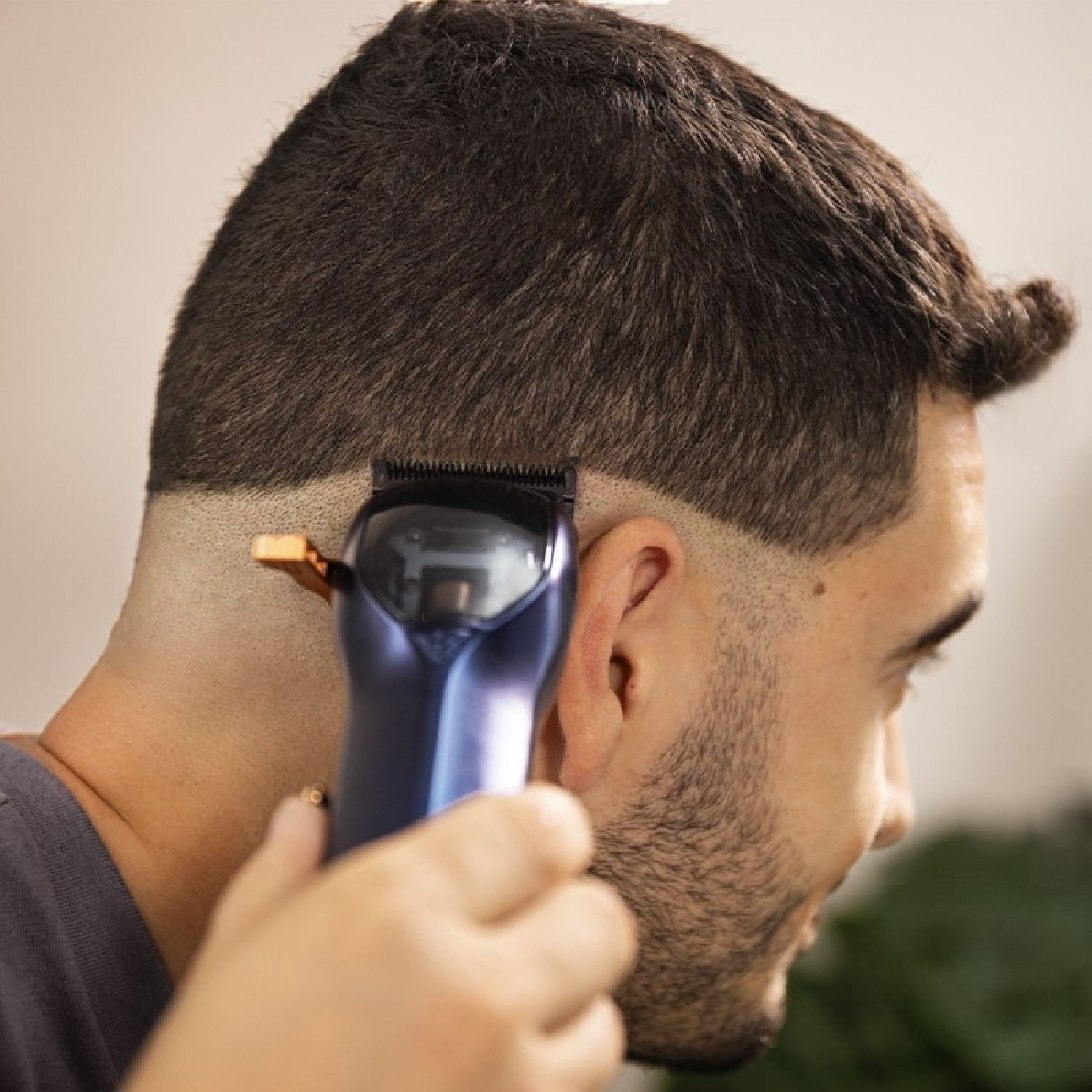 Una persona usa una máquina eléctrica azul para cortar el cabello corto y oscuro de un hombre.