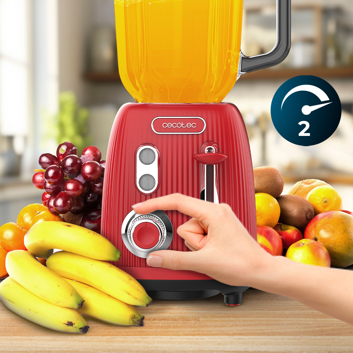 Mano che aziona un frullatore rosso circondato da frutta fresca come banane, uva e mele.