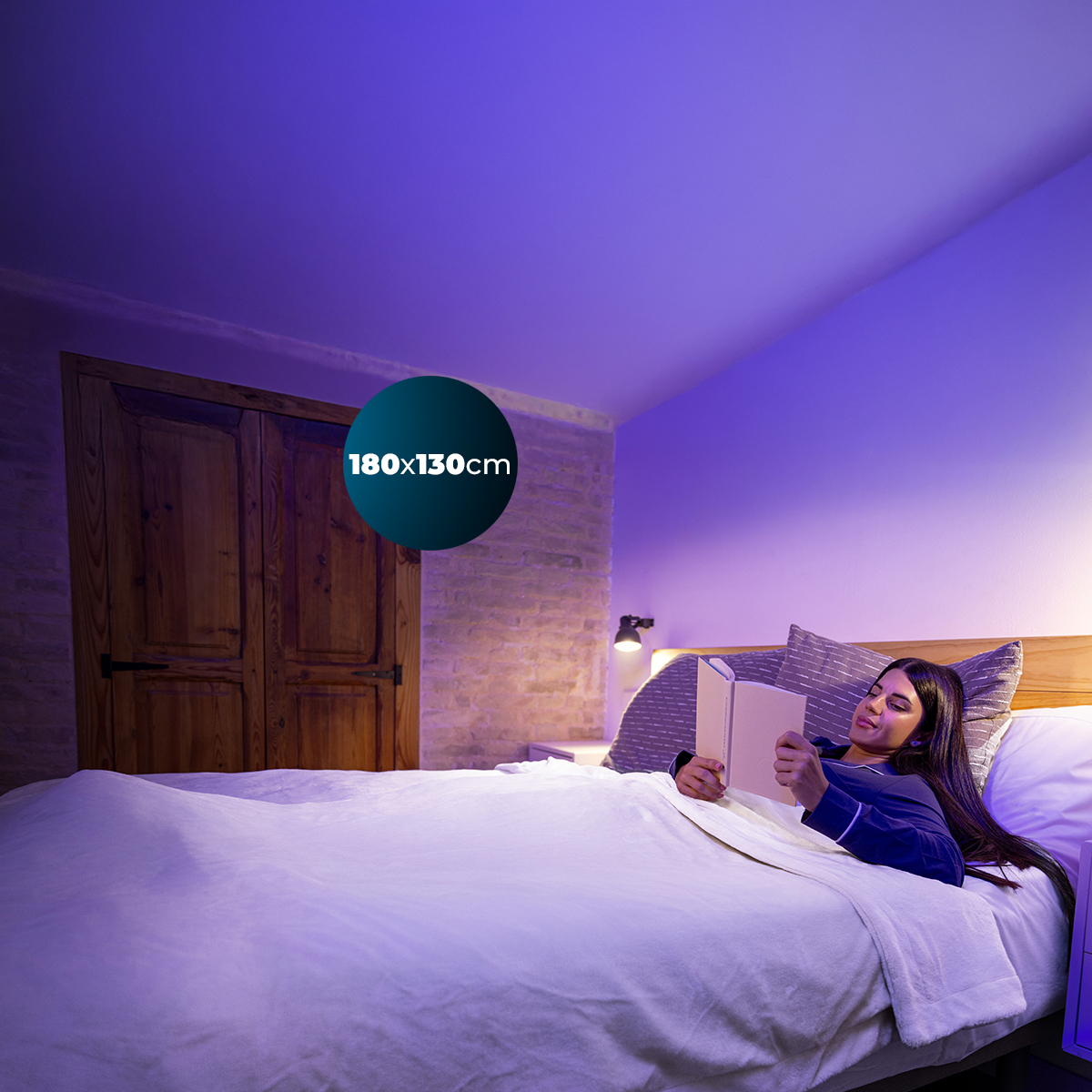 Una donna legge un libro a letto in una camera con luce viola.