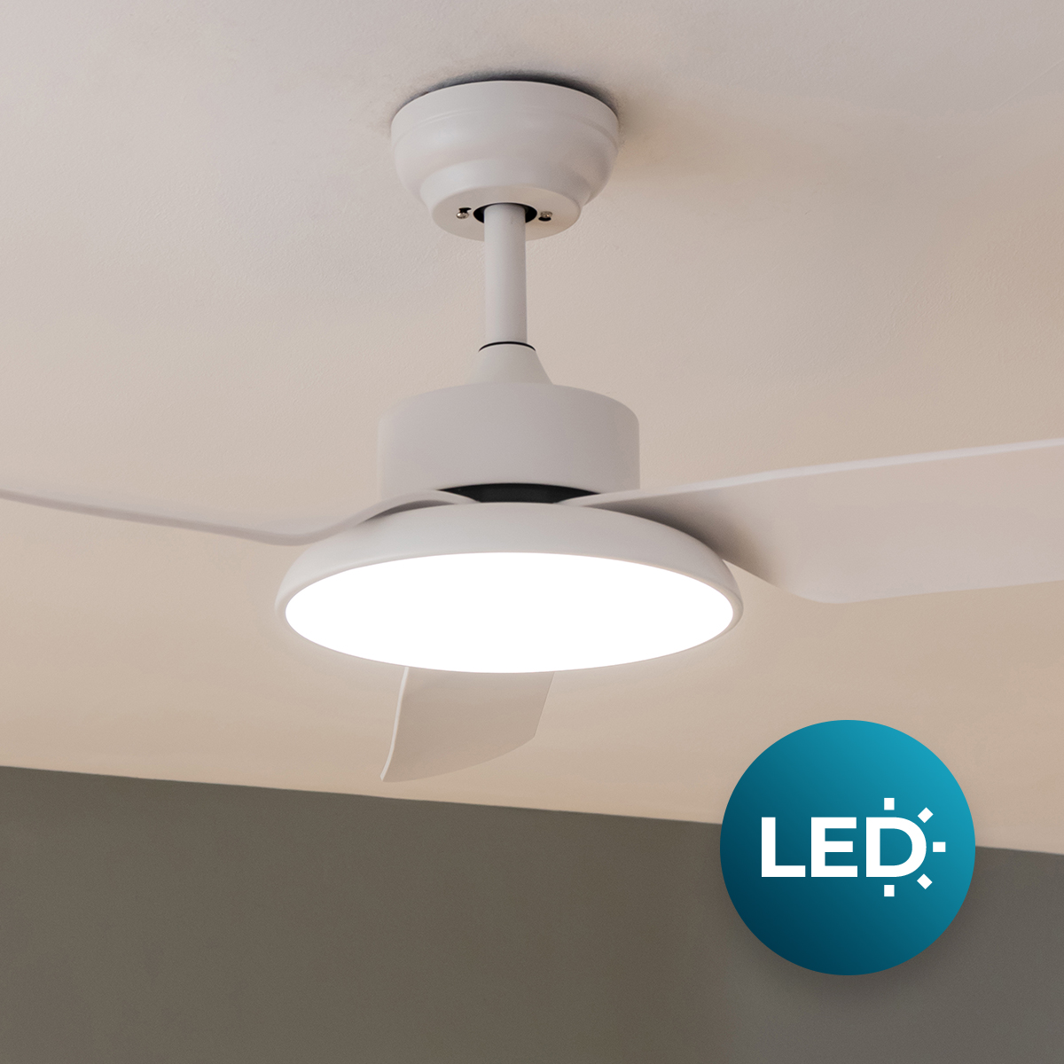 Un ventilador de techo blanco con una luz LED redonda integrada en la parte inferior está montado en un techo claro.