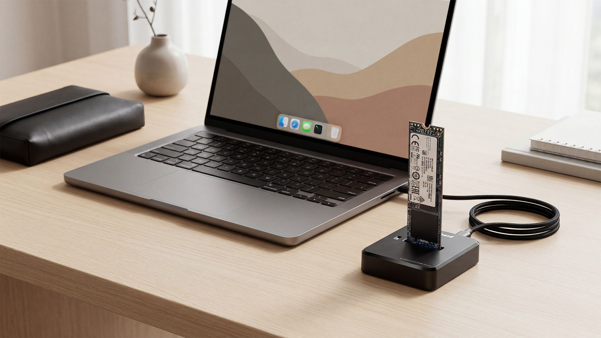 Dysk M.2 SSD podłączony przez czarną stację dokującą do laptopa na drewnianym biurku.