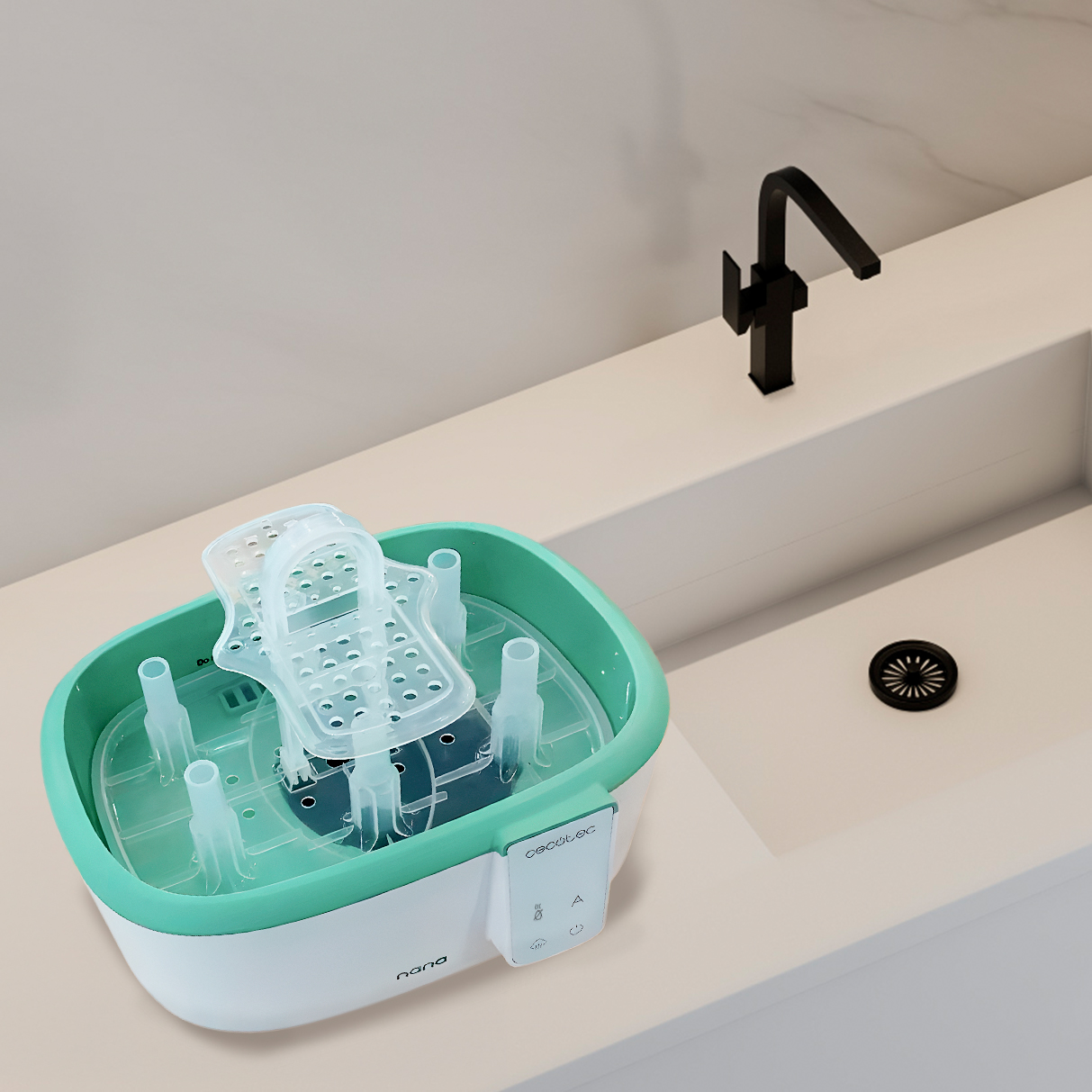 Un esterilizador de biberones blanco y verde azulado está sobre una encimera junto a un lavabo blanco con grifo negro.