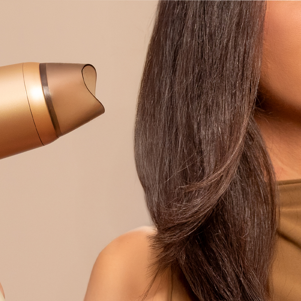 Un secador de pelo dorado sopla aire sobre el cabello largo y castaño oscuro de una persona.