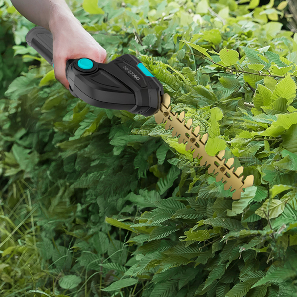 Mano sosteniendo un cortasetos inalámbrico negro con hoja dorada cortando hojas verdes.