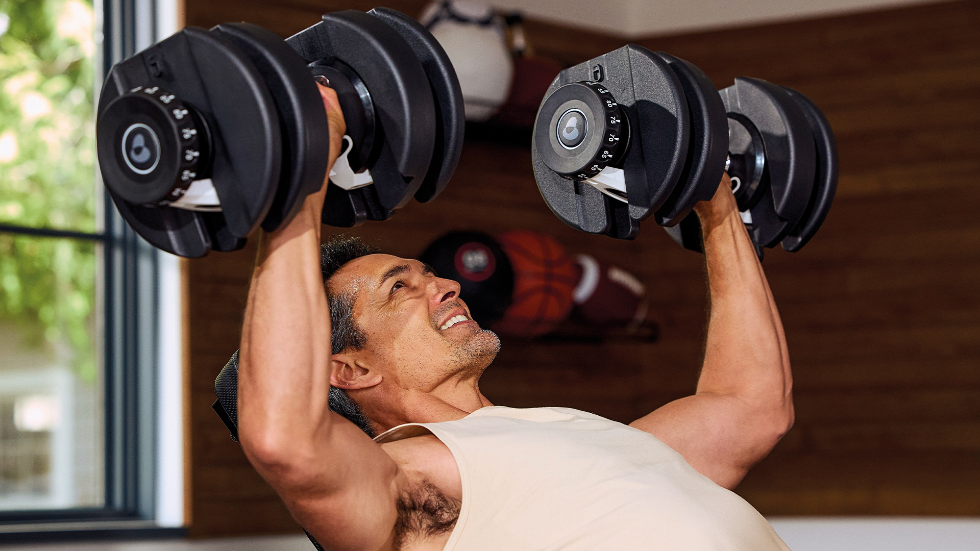 Ein Mann hebt in einem Fitnessstudio schwere verstellbare Hanteln beim Bankdrücken.